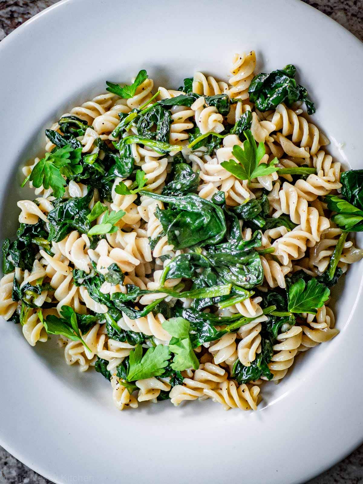 Top view of a large white bowl filled with spinach pasta and garnished with fresh parsley.