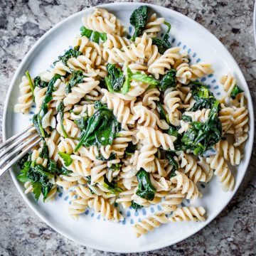 Pasta with sautéed spinach mixed together on a plate.