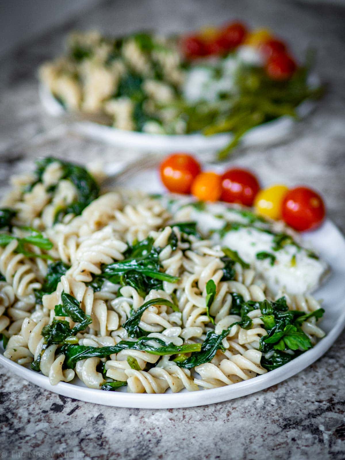 Spinach pasta on a white plate with fish and tomatoes.