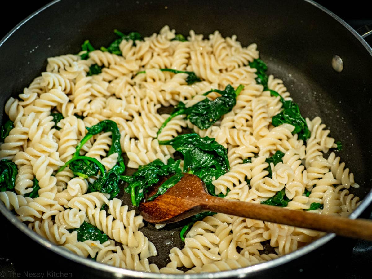 Spinach and pasta stirred together with a wooden spoon in a large skillet.