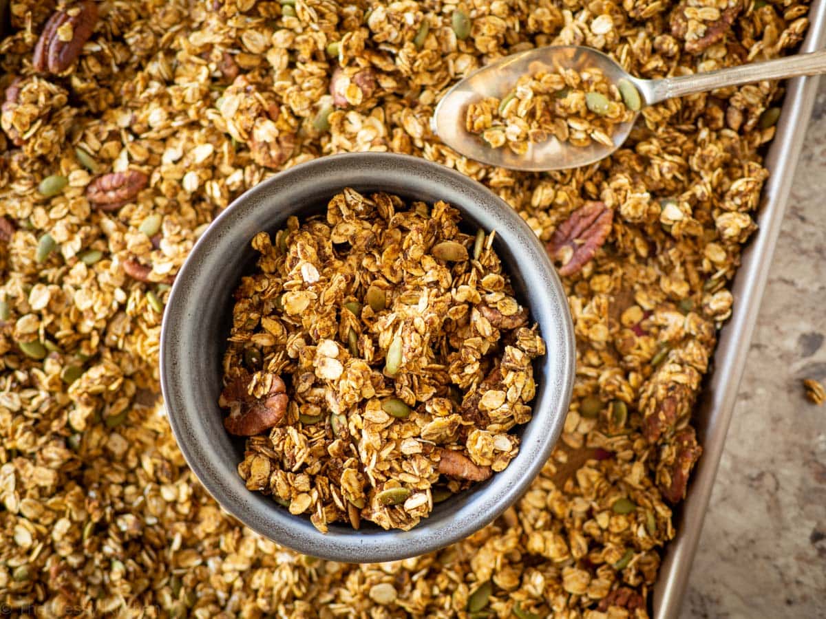 Bowl of pumpkin granola on top of a sheet pan filled with fresh baked granola.