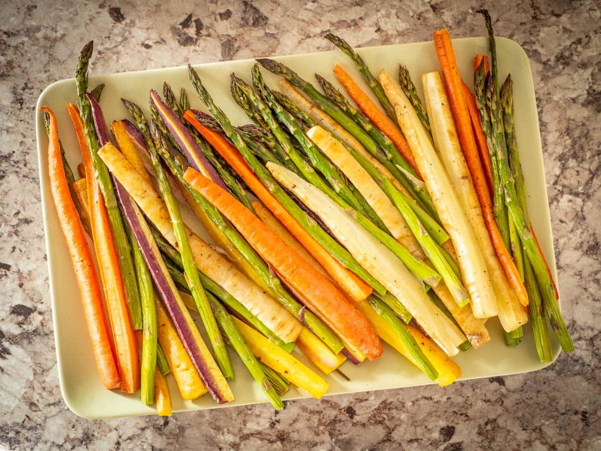 Top view of cooked carrot and asparagus spears on a green plate.