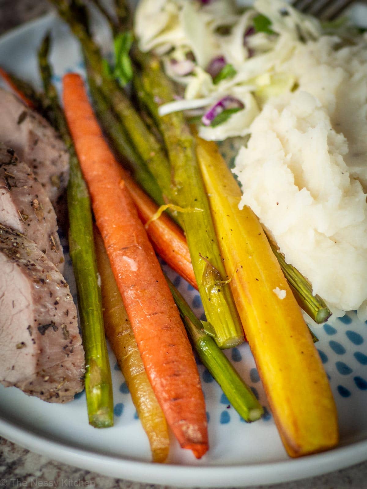 Carrots and asparagus on a plate with potatoes and pork.