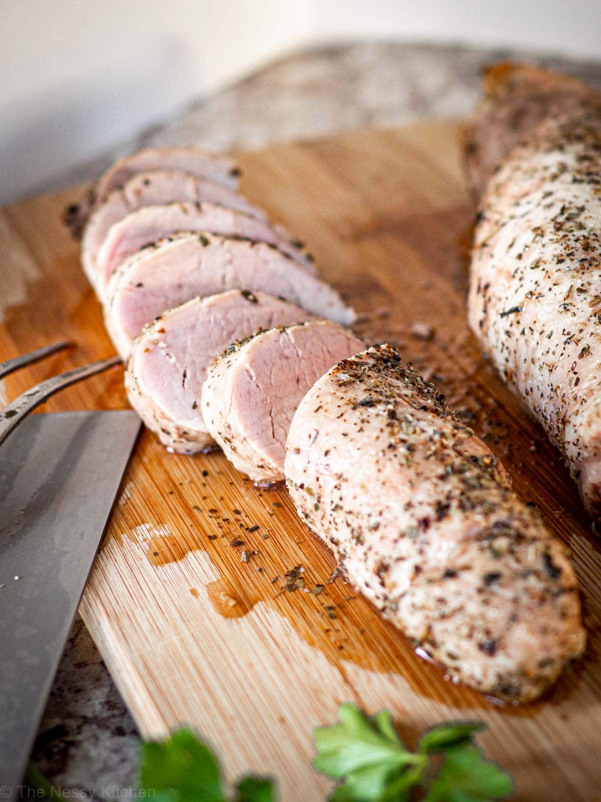 Sliced pork tenderloin on a wooden cutting board.