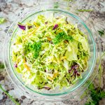 Bowl of sliced carrots and cabbage topped with a green sauce and fresh parsley.