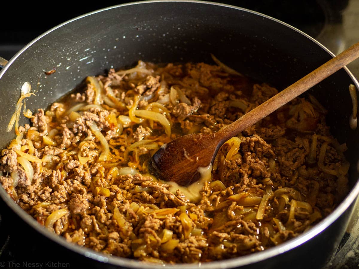 Sauce ingredients added to the skillet and stirred with a wooden spoon.