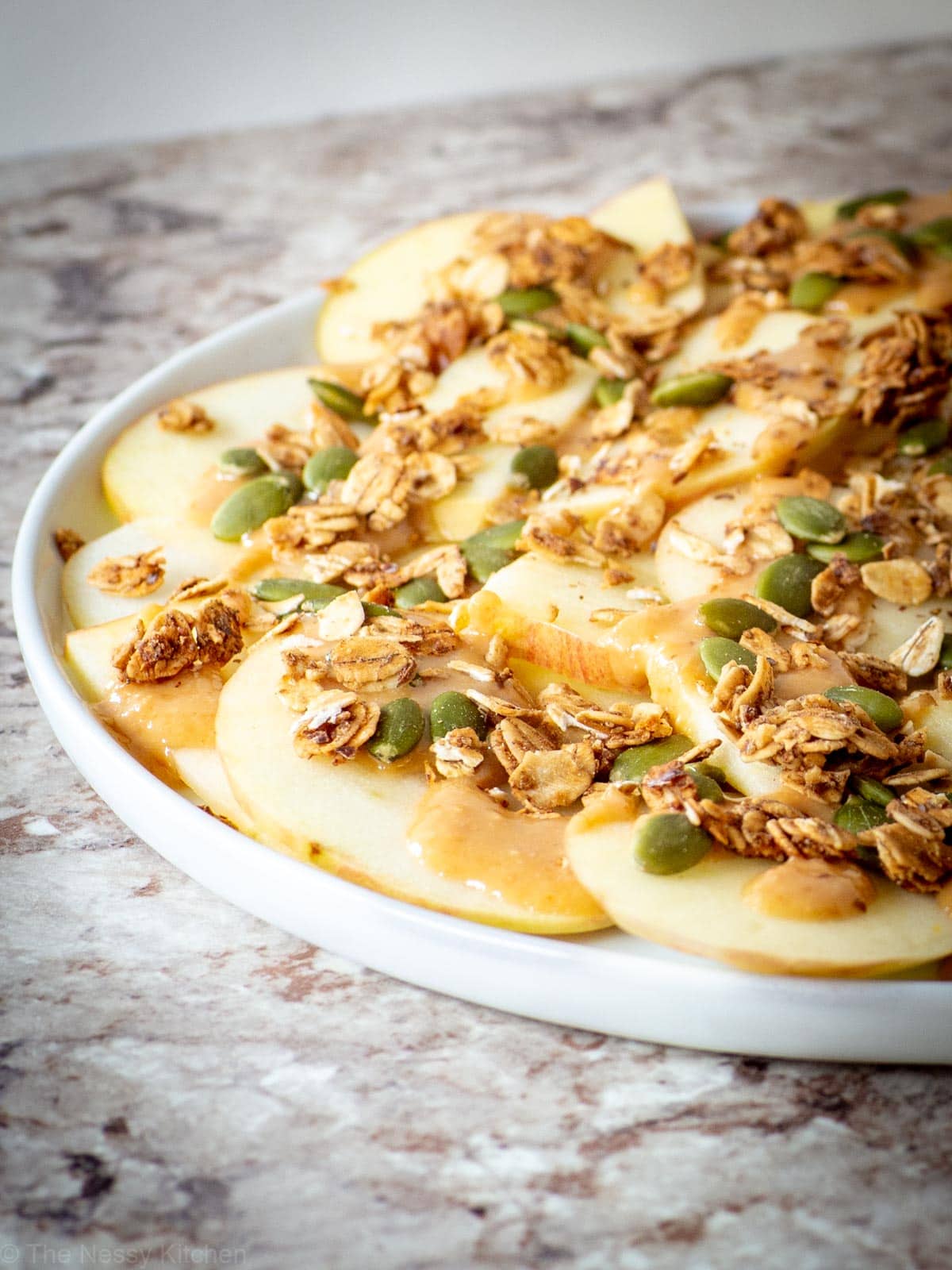Plate of thinly sliced apples topped with nut butter, granola and pumpkin seeds.