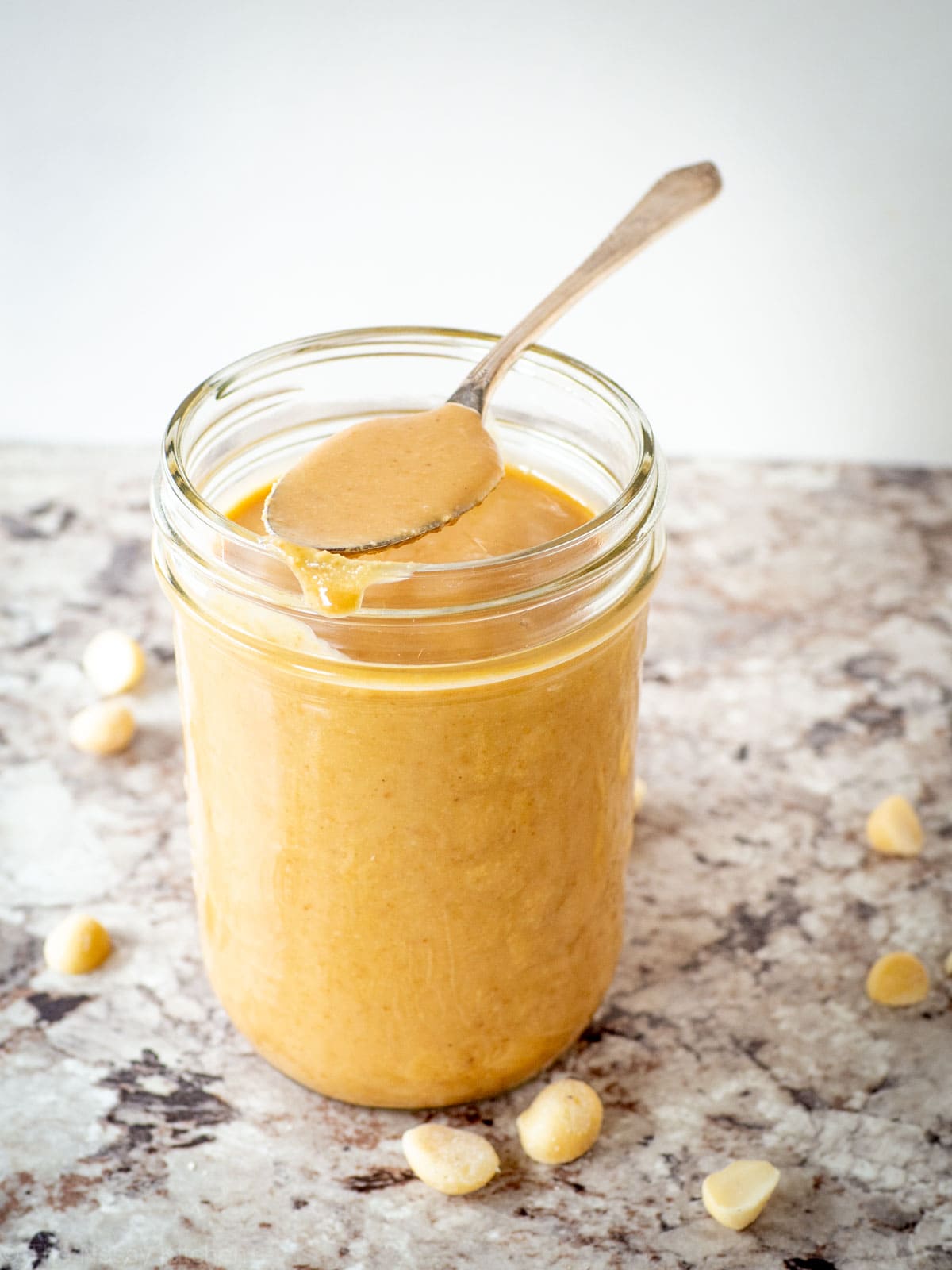 Mason jar of macadamia butter with a spoonful sitting on top.