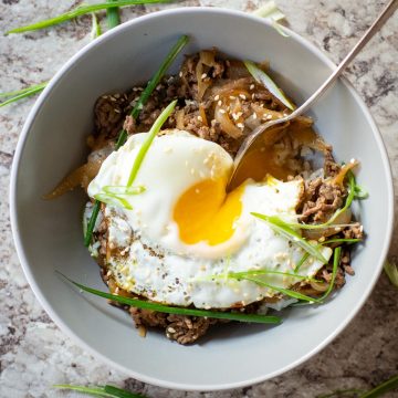 Ground beef and rice in a grey bowl topped with a sunny side up egg.