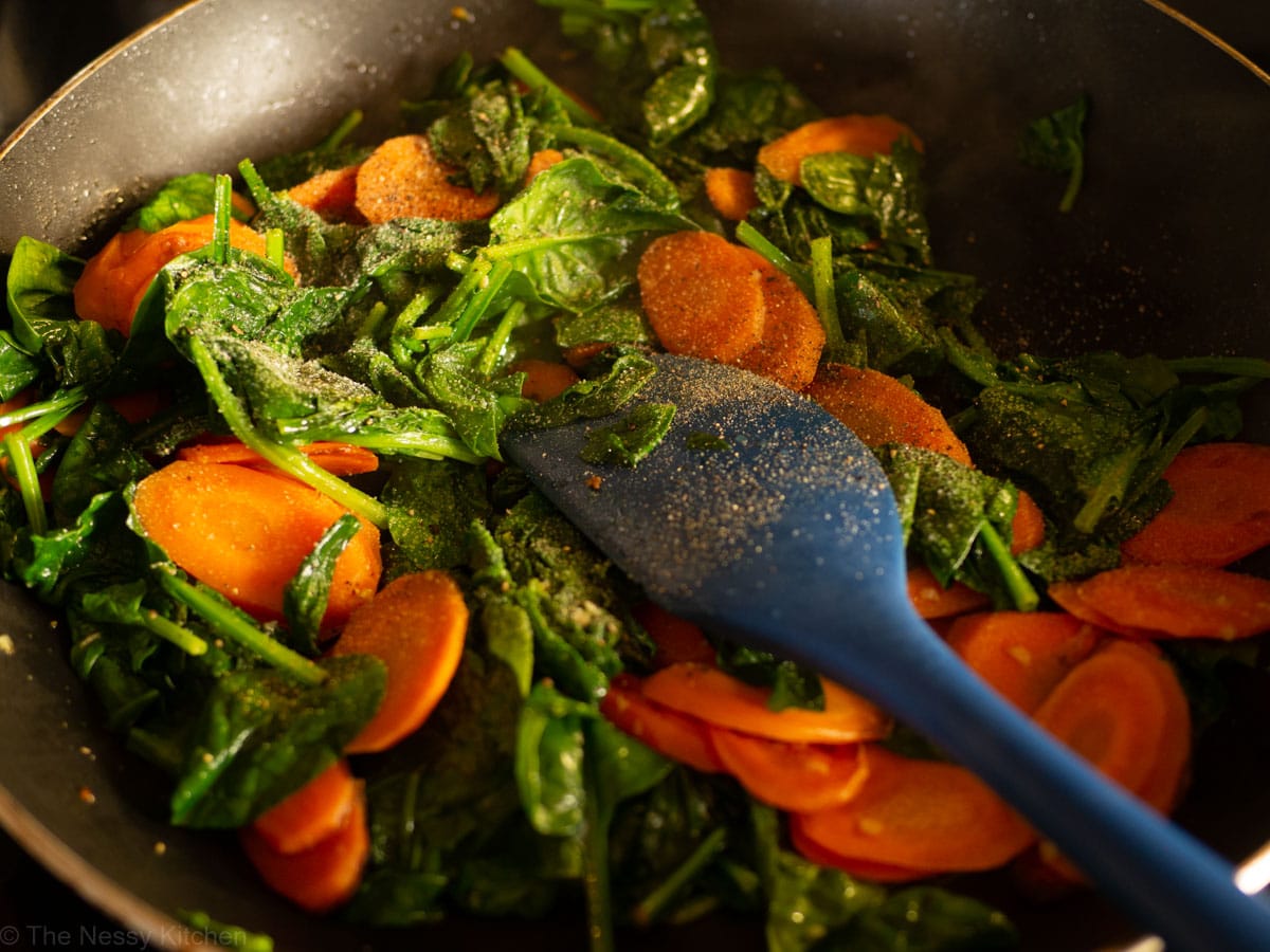 Salt and pepper sprinkled over cooked vegetables in a skillet.