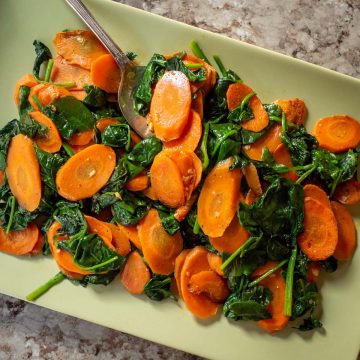 Green plate with carrots and spinach and a serving spoon.