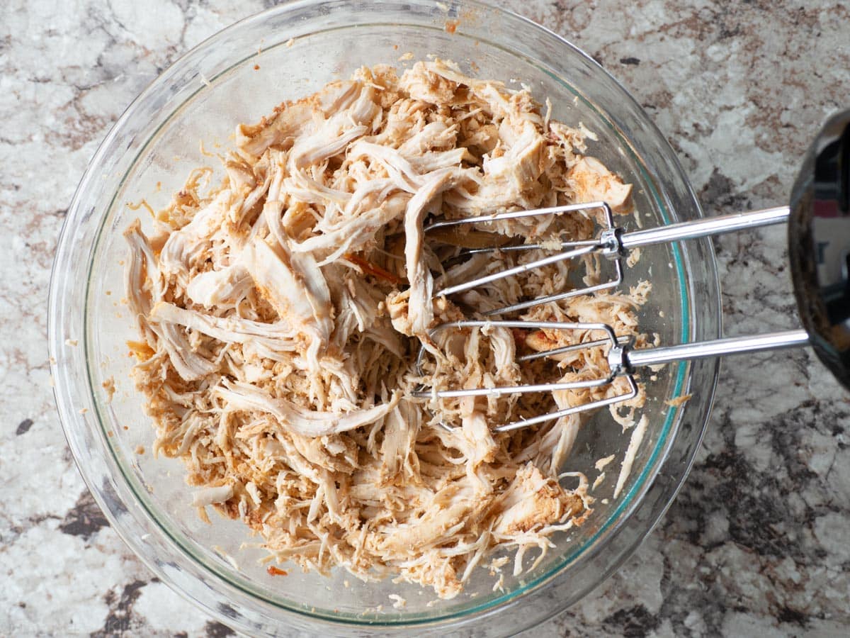 Chicken breasts shredded in a bowl with a hand mixer.