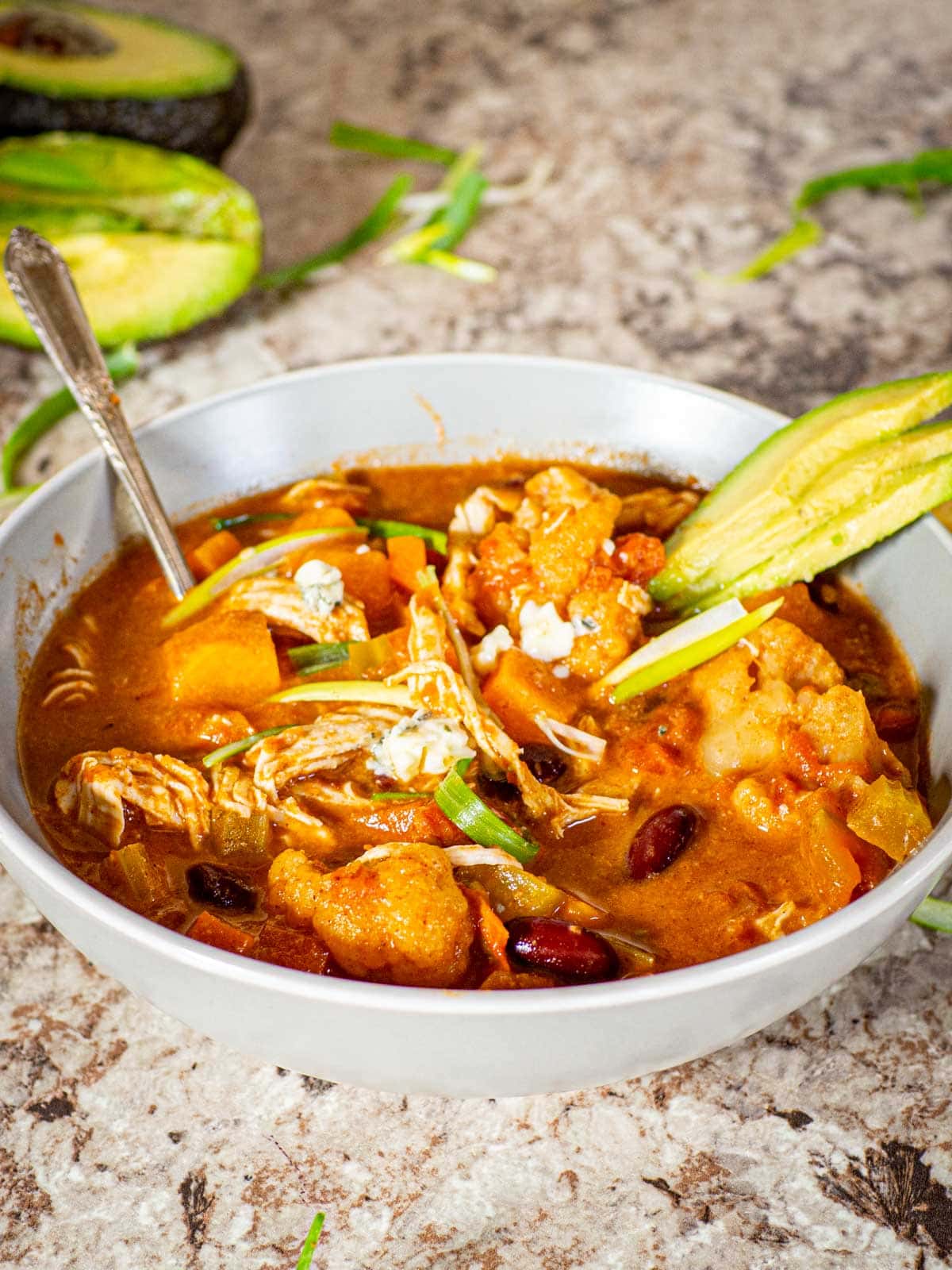 Bowl of buffalo chicken chili topped with avocado and sliced green onions.