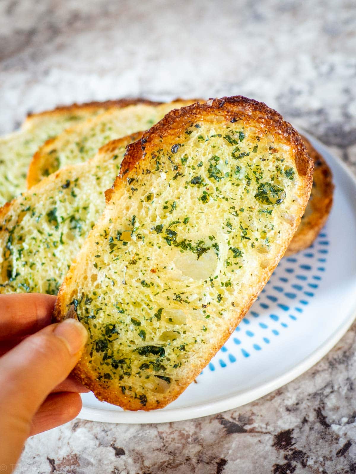 Hand holding up a piece of garlic bread.