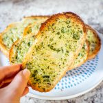 Hand holding up a piece of garlic toast.