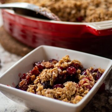 Bowl of cranberry crisp with a baking dish in the background.