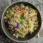 Coleslaw mix with ground pork in a grey bowl over rice.