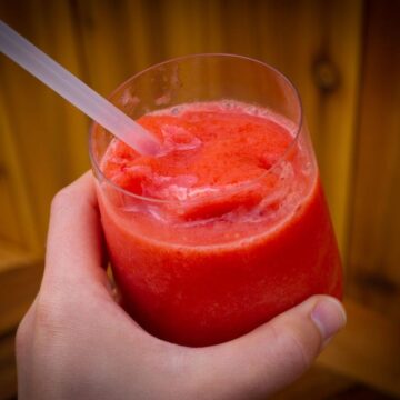 Hand holding a glass of a pink frozen drink with a straw.