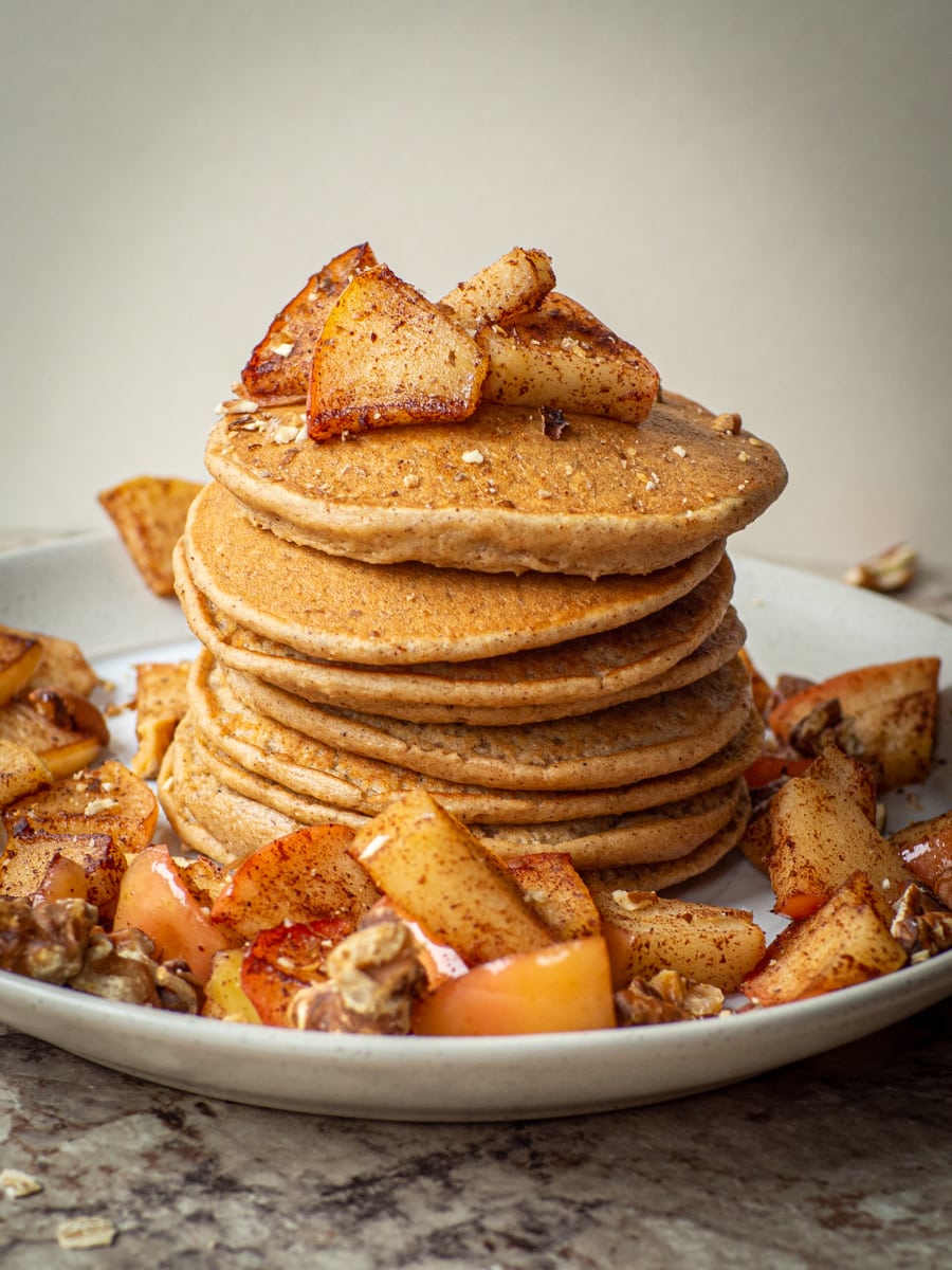 Stack of pancakes on a plate topped with cooked apples.