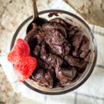 Bowl of brownie batter with a spoon and topped with sliced strawberries.
