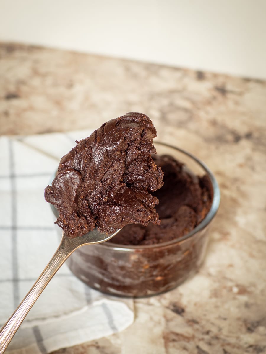 Spoonful of edible brownie batter with a bowl in the background.