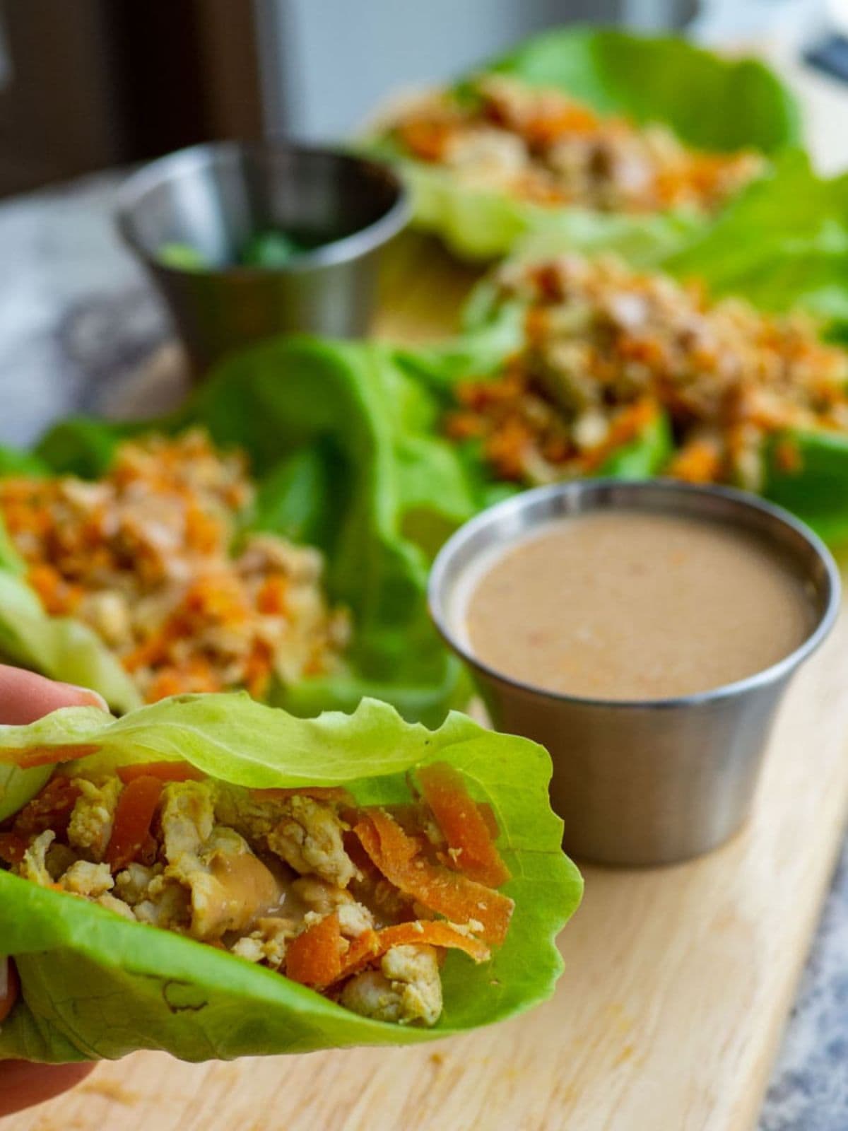 Hand holding up a turkey lettuce wrap topped with peanut sauce.