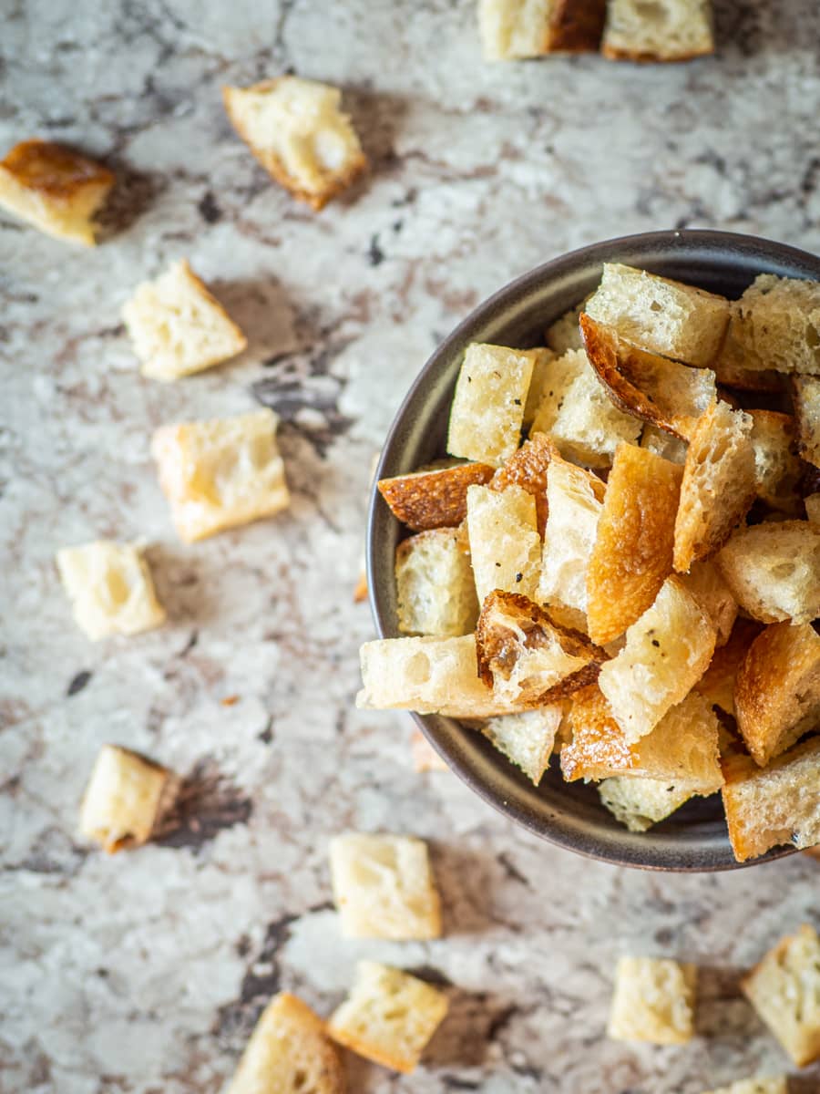 Bowl of croutons with some on stray bites on the counter.