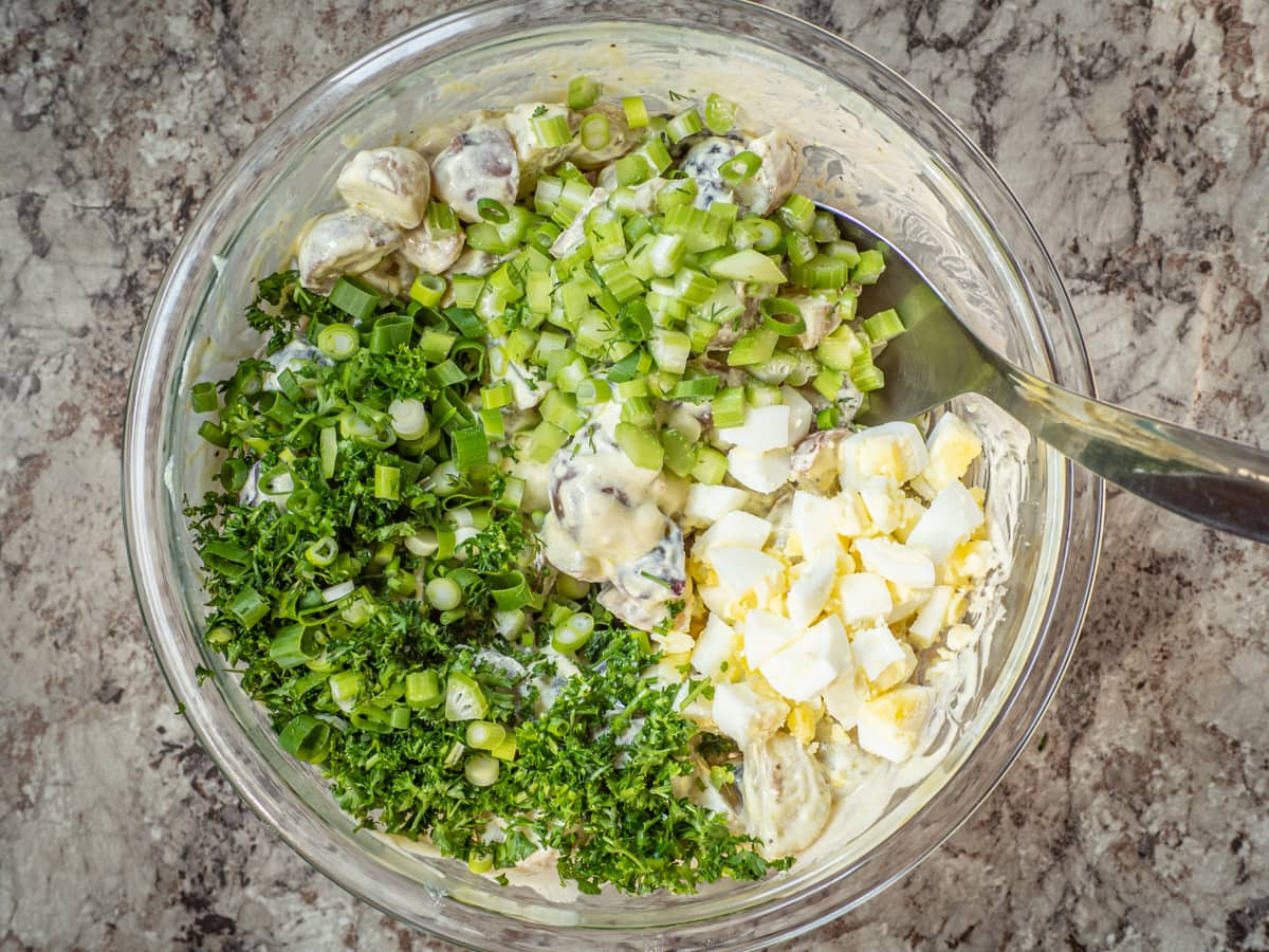 Herbs, celery and eggs added to a bowl with potatoes.