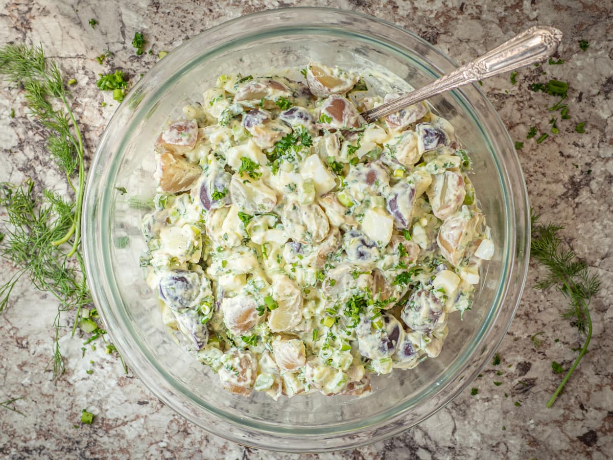 Mixed bowl of potato salad with a serving spoon.