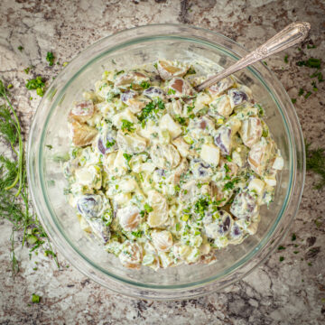 Bowl of creamy potato salad topped with herbs.
