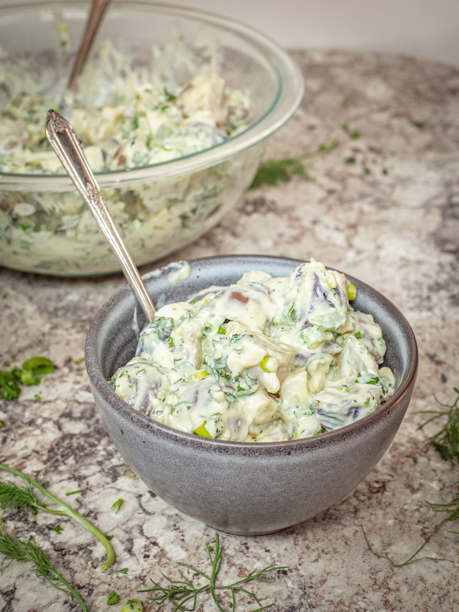 Grey bowl of potato salad with a spoon.