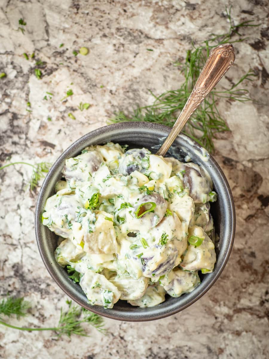 Top view of a bowl of Greek yogurt potato salad topped with fresh herbs.