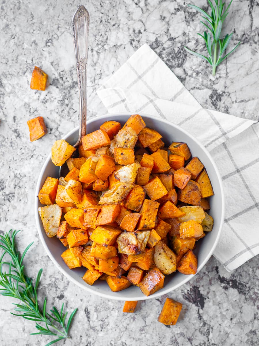 Bowl of roasted sweet potatoes and apples with a serving spoon.