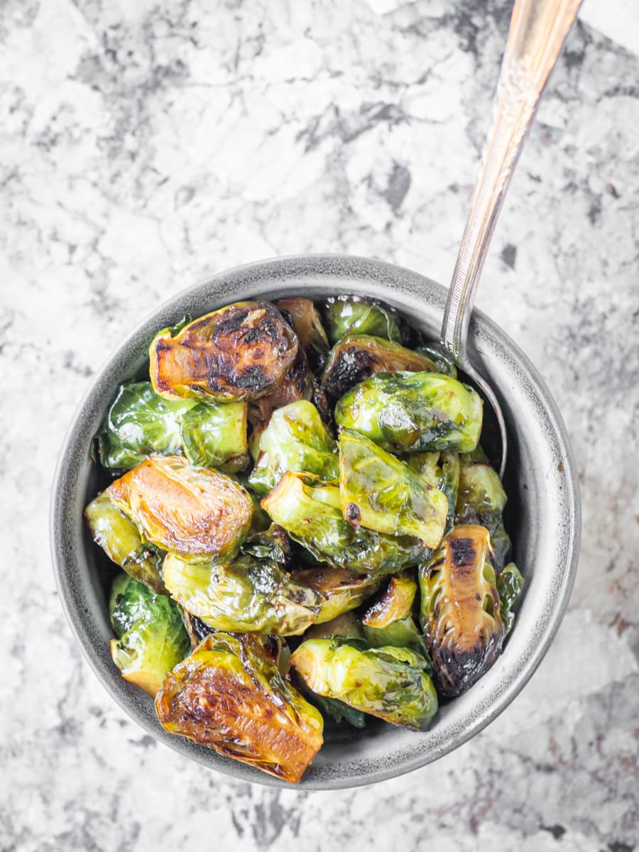 Gray bowl mixed of balsamic sautéed Brussels sprouts with a serving spoon.