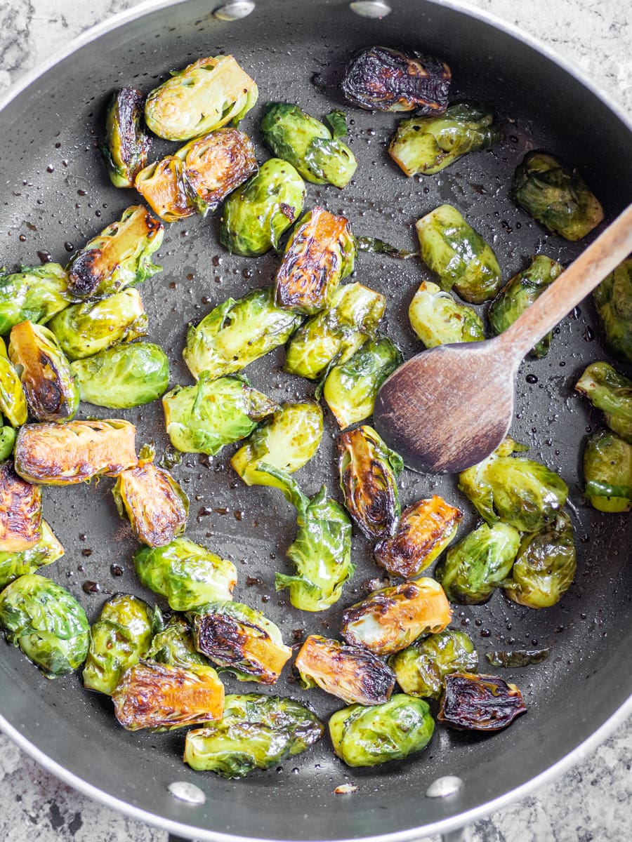 Skillet with sautéed brussels sprouts and a wooden spoon.