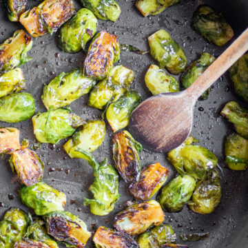 Balsamic sautéed Brussels sprouts in a skillet with a spoon.