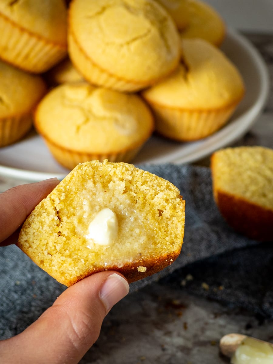 Hand holding a buttered cornbread muffin.