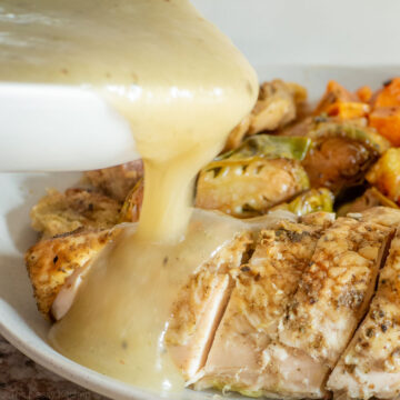 Gravy being poured onto a piece of roasted chicken.