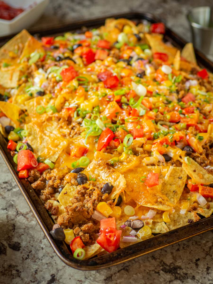 Nachos on a baking sheet topped with tomatoes and green onions.