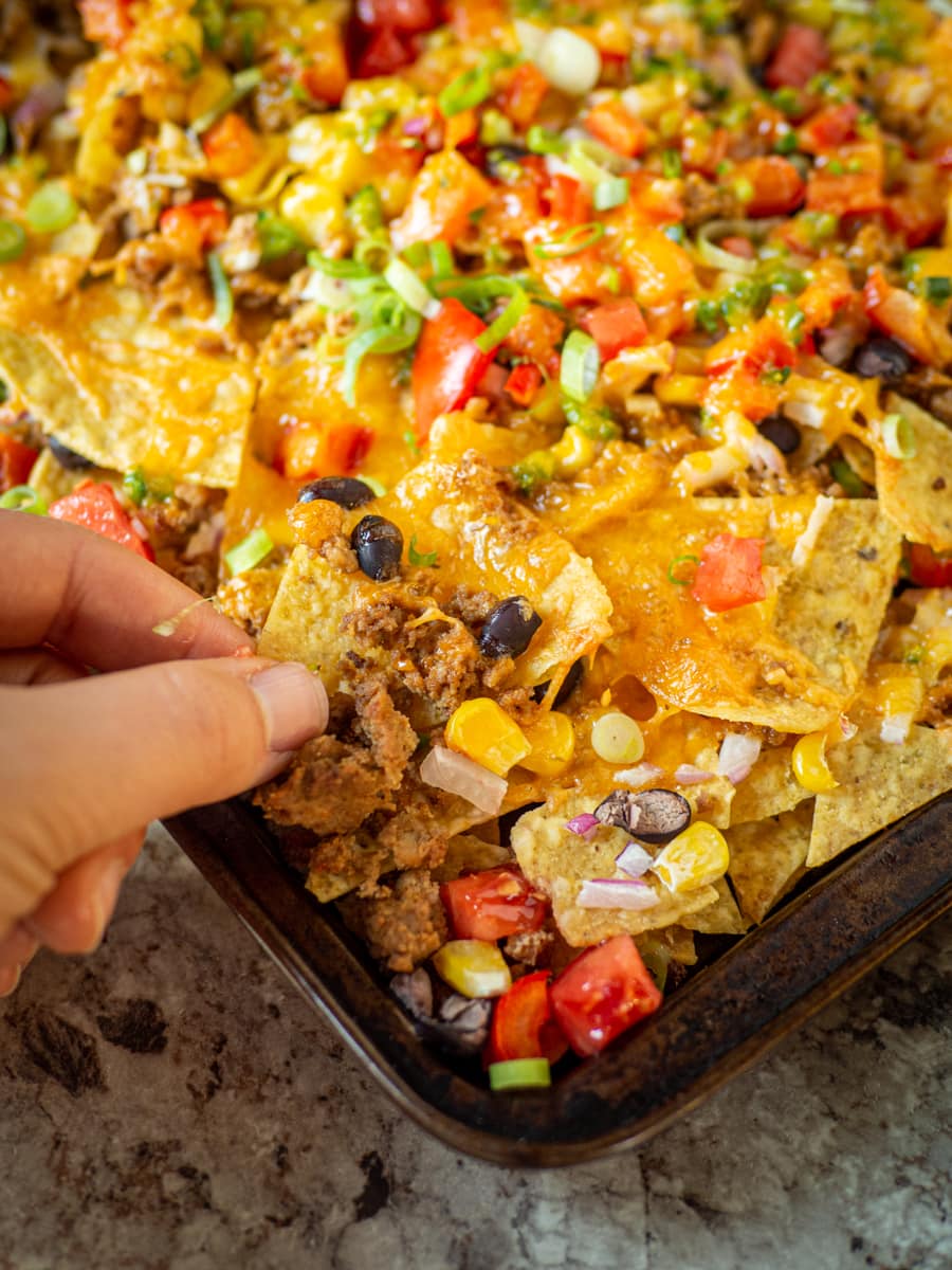 Hand grabbing a chip off of a pan of nachos.