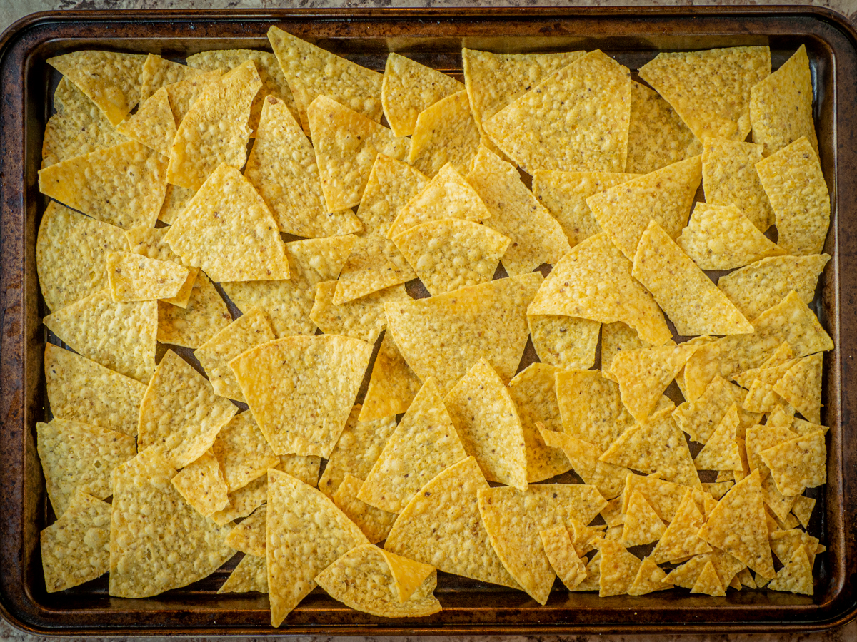 Tortilla chips spread out on a sheet pan and overlapping slightly.