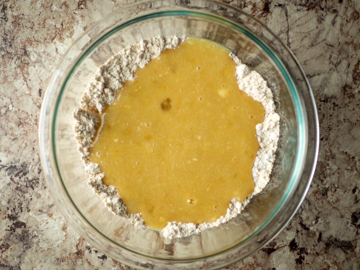 Wet and dry muffin batter ingredients being combined in a glass bowl.