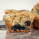 Blueberry muffin with a bite taken out sitting on a countertop.