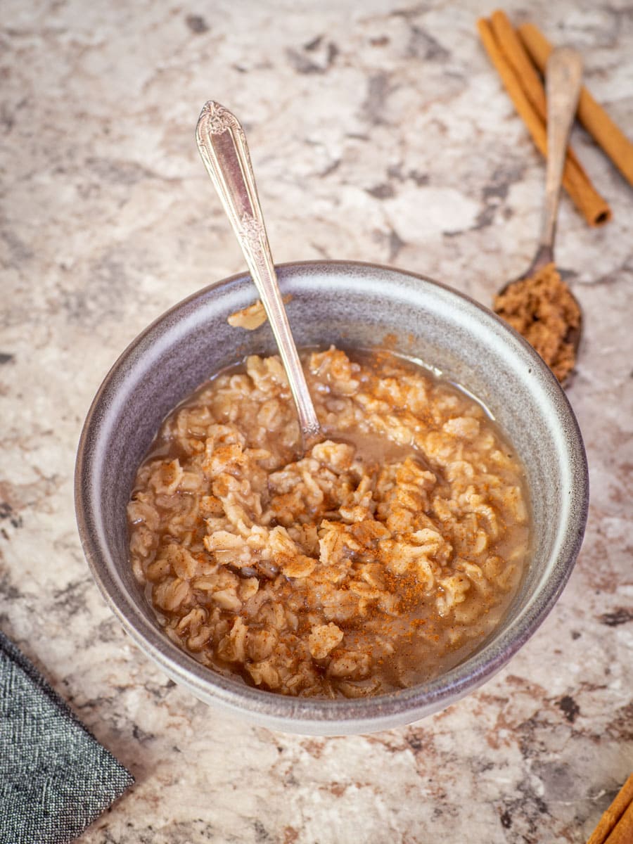 Bowl of oatmeal with brown sugar and cinnamon in the background.