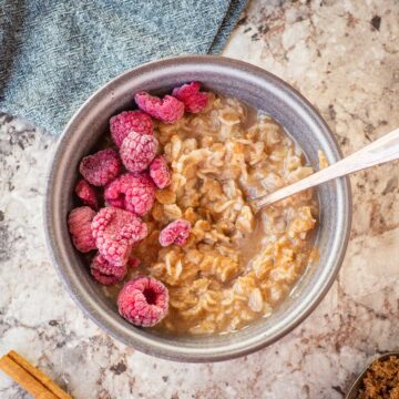 Bowl of oatmeal topped with cinnamon and raspberries.