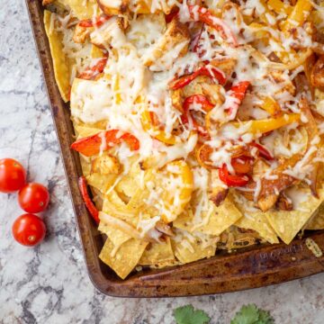 Sheet pan of nachos topped with chicken, peppers and cheese.