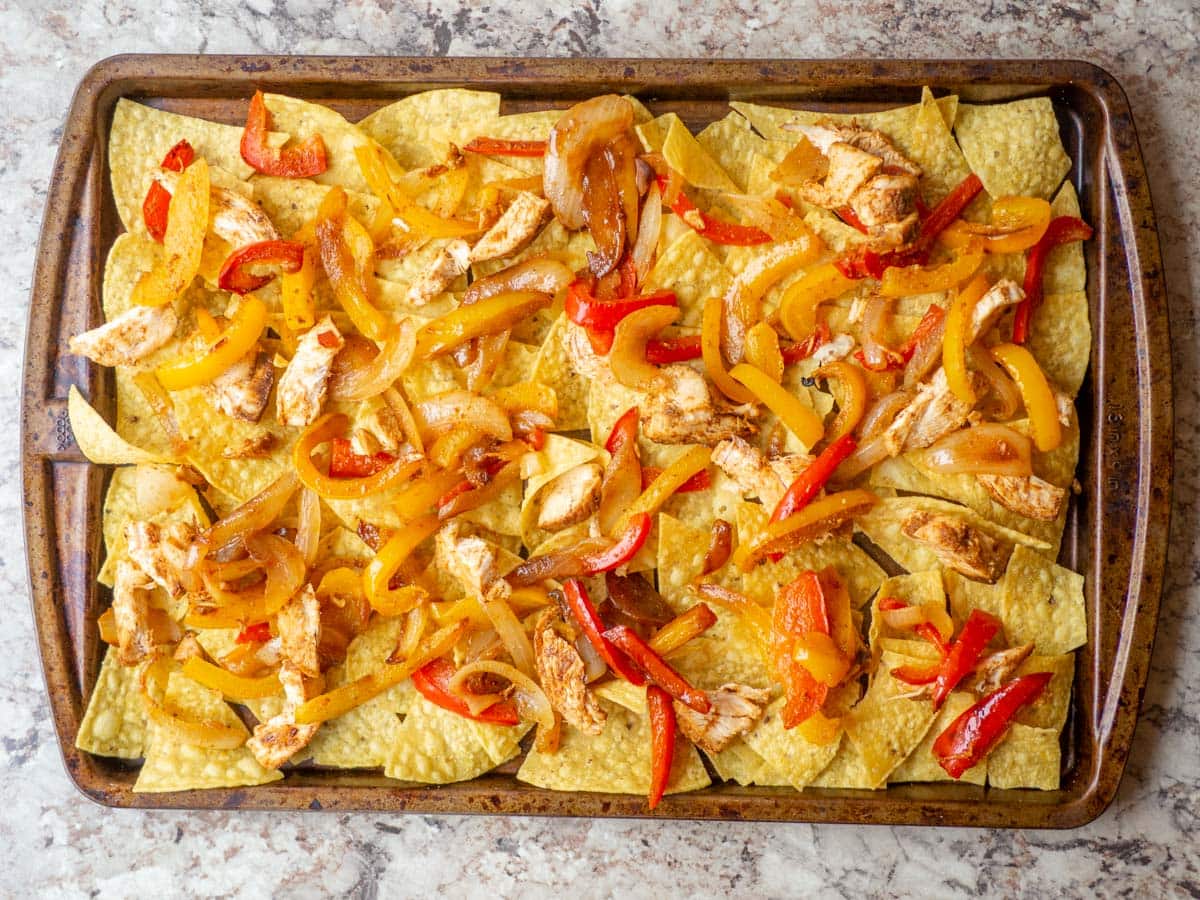 Onions, peppers and chicken spread out on a sheet pan of tortilla chips.