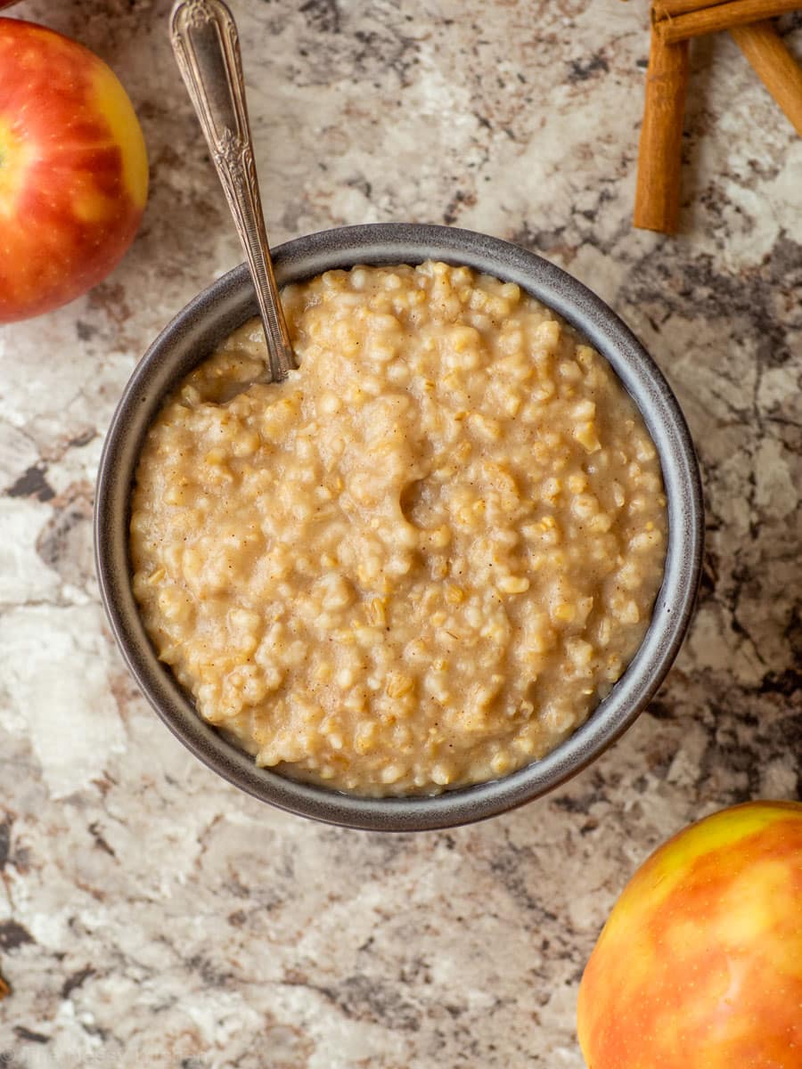Bowl of oatmeal with a spoon next to apples.