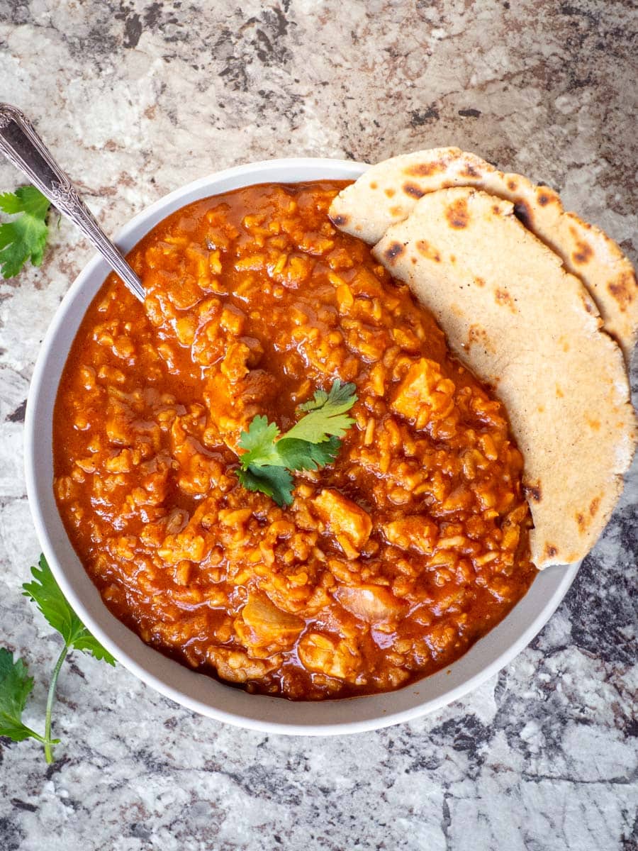 Bowl of chicken tikka masala garnished with cilantro with a side of naan.