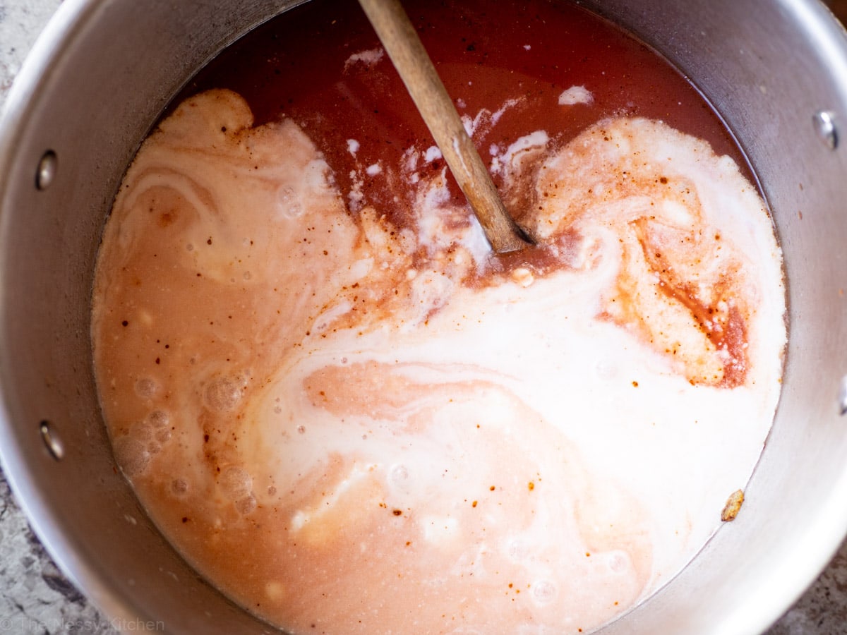 Tomatoes and coconut milk stirred together in a pot.